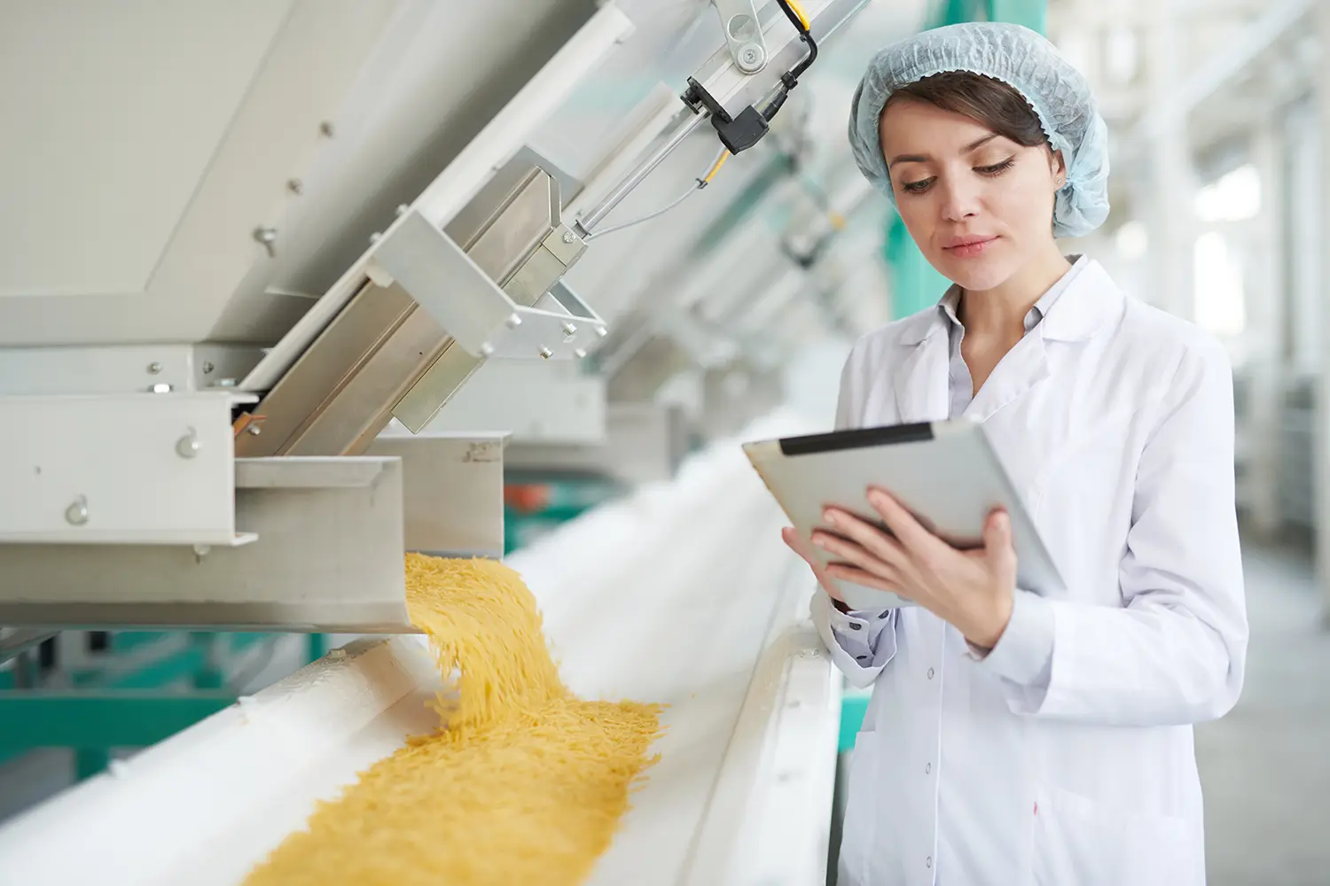Waist up portrait of young woman standing by machines and using digital tablet while inspecting macaroni production at food factory , copy space